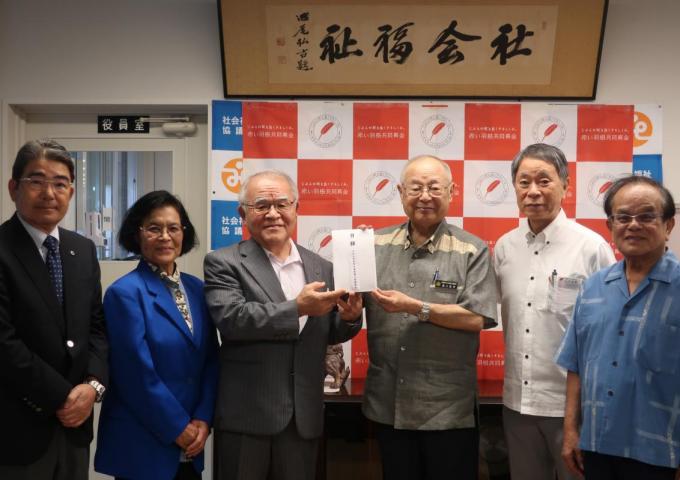 県民生委員児童委員協議会の屋宜恒一会長(左から3人目)から県共同募金会の湧川昌秀会長(同4人目)へ寄附目録を贈呈